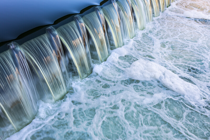 Wasser fließt über einen Damm und erzeugt schäumende Strudel darunter.