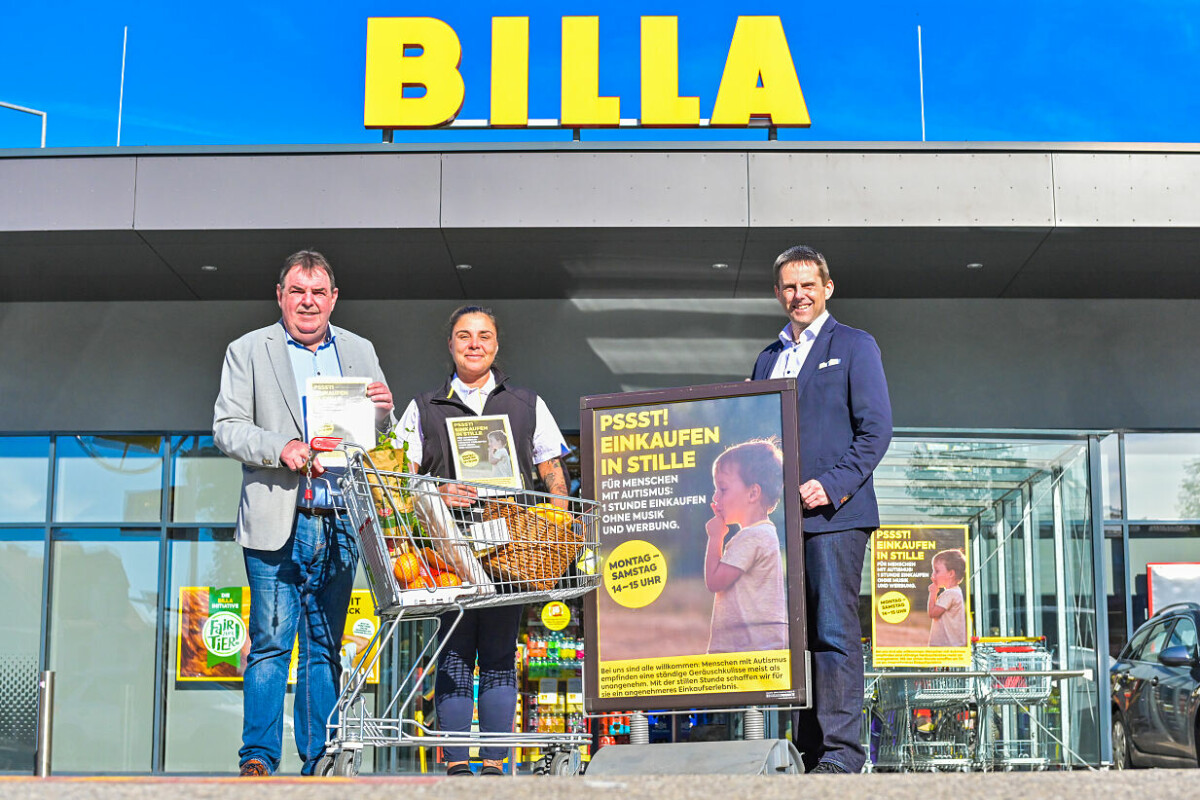 Drei Personen stehen vor einem Billa-Supermarkt. Zwei Einkaufswagen sind mit Lebensmitteln gefüllt. Ein Plakat informiert über das Einkaufen in Stille. Im Hintergrund ist das Billa-Logo zu sehen.