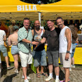 BILLA-Stand bei einem Fest in Wien mit vier Männern, die sich umarmen.