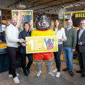 Eine Gruppe von fünf Personen steht in einem Supermarkt neben einem Wildschweinmaskottchen. Sie halten ein Schild mit dem Text "Los für Vereine BILLA" und dem Logo von "Österreichische Lotterien" und "Glücksbringer". Im Hintergrund sind Regale und BILLA-Werbung zu sehen. Alle Personen lächeln in die Kamera.