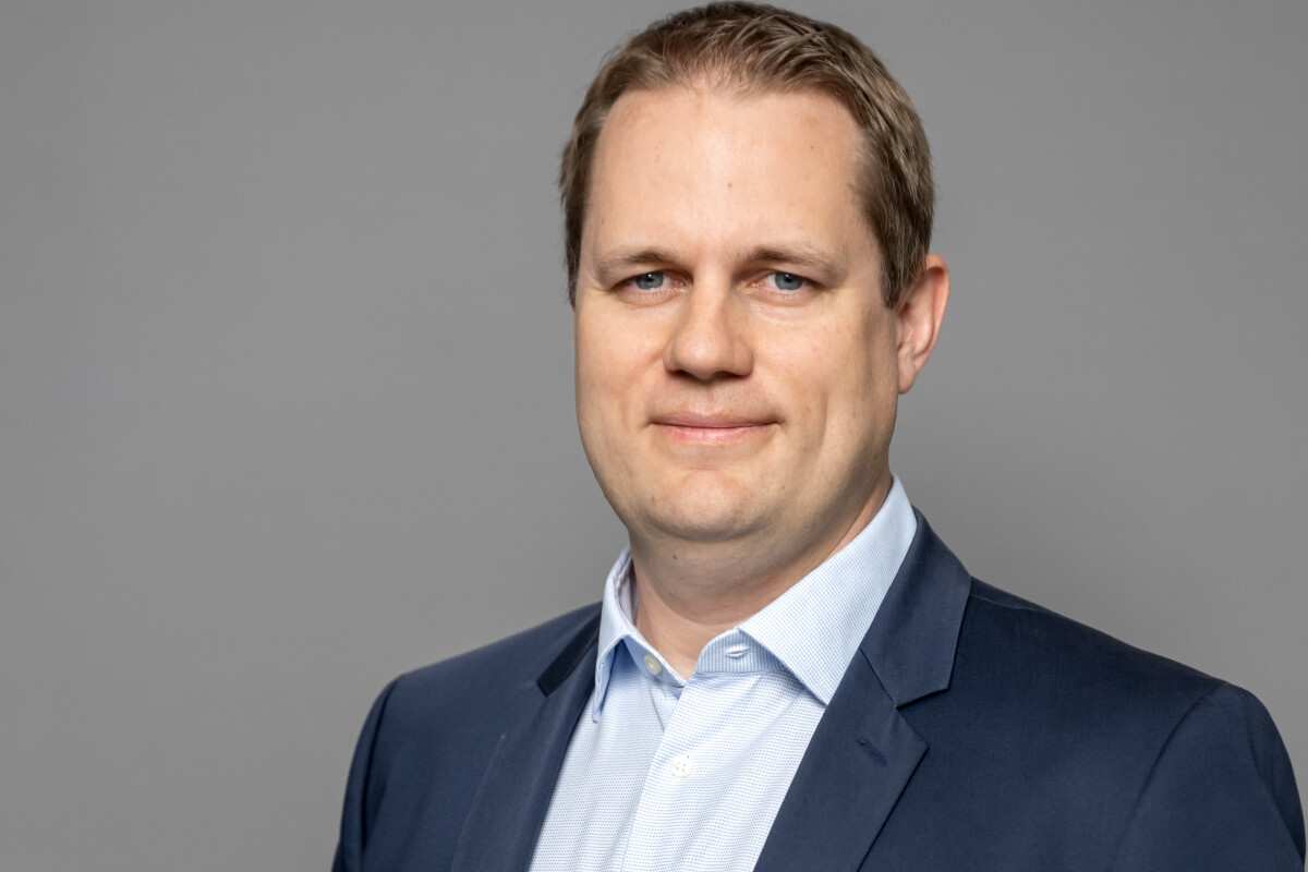 Ein Mann in einem blauen Anzug und einem hellblauen Hemd vor einem grauen Hintergrund.