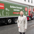 Ein Mann steht vor einem Lastwagen mit der Aufschrift "Grüne Energie voraus" und dem Penny-Logo. Der Lastwagen ist auf einer städtischen Straße geparkt.