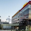 Moderne Gebäude mit Glasfassade und den Logos von REWE und BILLA, bei Sonnenuntergang.