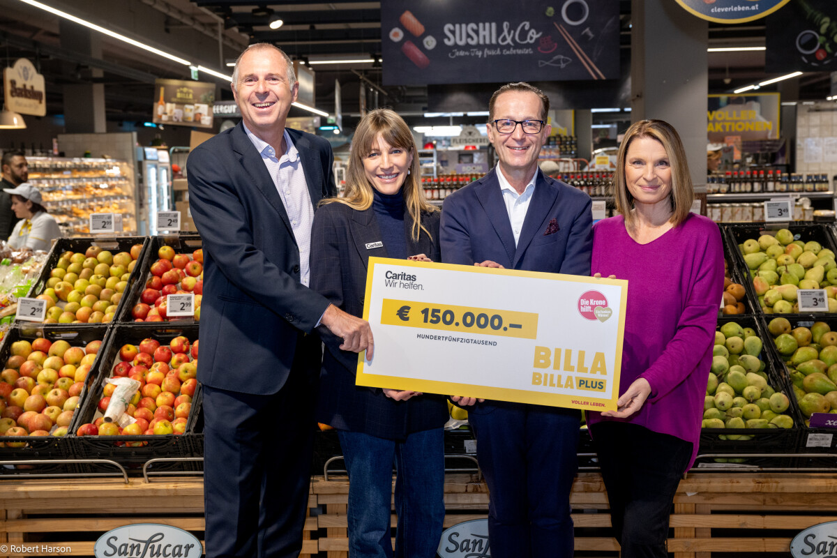 Vier Personen halten einen symbolischen Scheck über 150.000 Euro. Im Hintergrund ist ein Supermarkt mit Obst ausgestellt. Alle Personen lächeln in die Kamera.