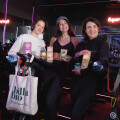 Drei Frauen stehen in einem Fitnessstudio, umgeben von Indoor-Cycling-Fahrrädern. Eine Frau hält eine Tasche mit der Aufschrift "billa bio". Alle tragen Sportbekleidung und lächeln, während sie Lebensmittelprodukte in den Händen halten. Im Hintergrund ist das beleuchtete Logo "superCycle" zu sehen.