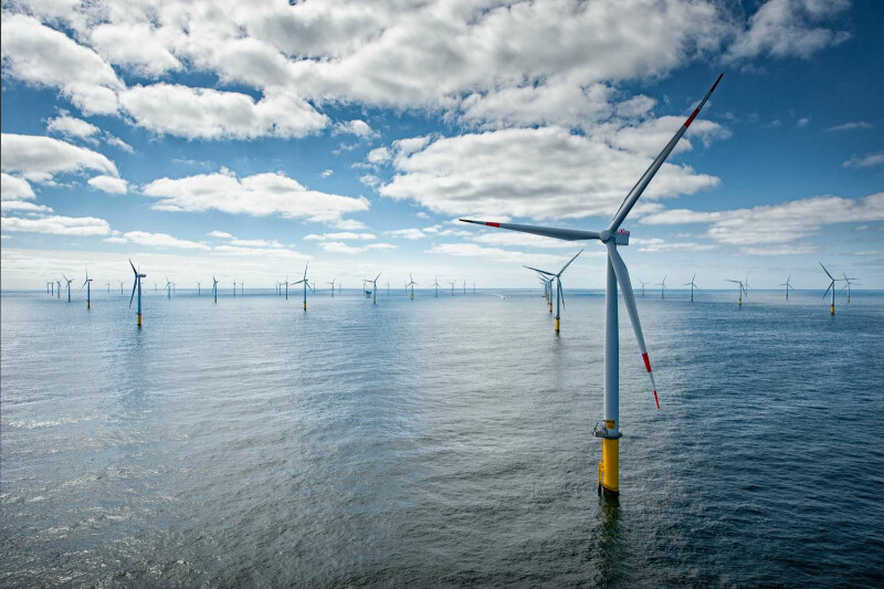 Mehrere Offshore-Windturbinen, die in einem großen Gewässer unter einem blauen Himmel mit vereinzelten Wolken stehen.
