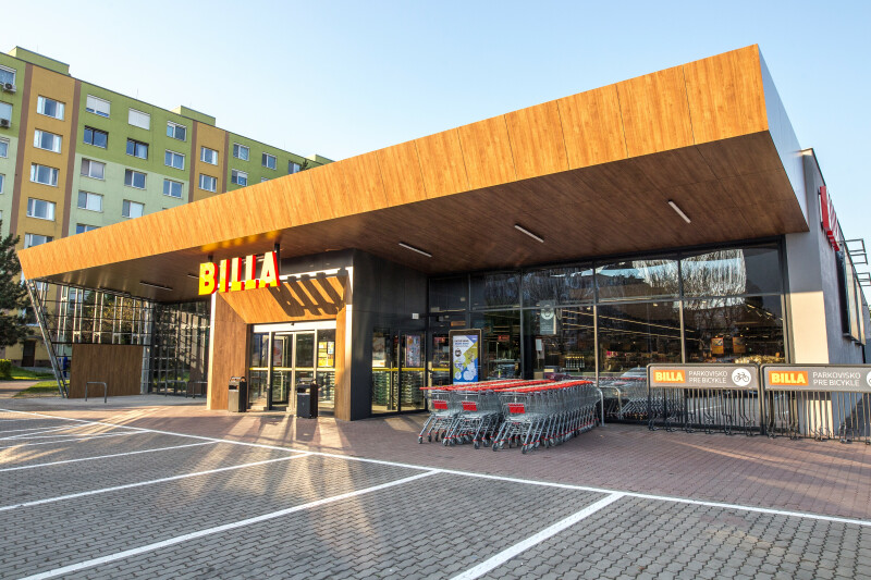 Ein moderner Supermarkt mit dem Logo "Billa" über dem Eingang und Einkaufswagen davor. Im Hintergrund sind Wohngebäude zu sehen.