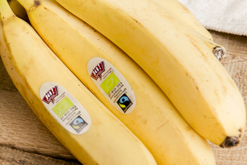 A bunch of bananas with stickers, including a Fairtrade certification, on a wooden surface.