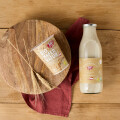 A bottle of plant-based milk and a cup of organic oat yogurt are placed on a wooden surface. Next to them is a round wooden board with two wheat stalks and a red cloth partially underneath.