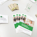 Brochures and cards promoting "Für Inklusion am Arbeitsmarkt" are arranged on a table, accompanied by branded pens.