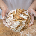 Hands holding a freshly baked rustic bread loaf with a crusty, flour-dusted surface.