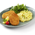 A plate with two breaded cutlets, a serving of potato salad garnished with chives, fresh greens, a cherry tomato, and a lemon wedge.