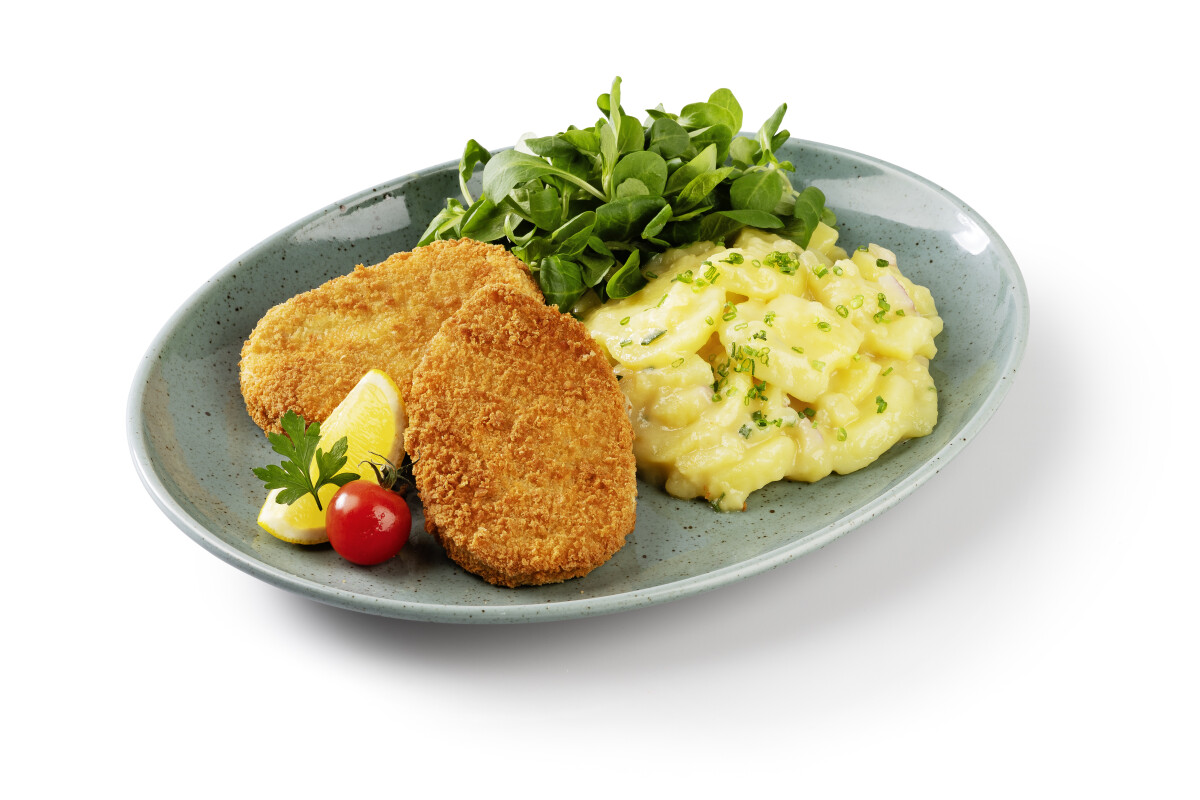 A plate with two breaded cutlets, a serving of potato salad garnished with chives, fresh greens, a cherry tomato, and a lemon wedge.