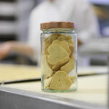A jar filled with heart-shaped cookies sits on a kitchen counter, with a person working in the background.
