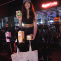 A woman in athletic wear poses in a cycling studio, holding cartons of billa bio products. She stands next to a stationary bike with a billa bio tote bag hanging from the handlebars. A neon sign reads “SuperCycle” in the background.
