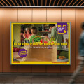 A person walking past a wall advertisement for Billa Online Shop. The ad features a brown paper bag with fresh groceries like lettuce, tomatoes, and bananas. The text promotes easy online shopping with a free 30-minute delivery offer. The background shows a kitchen scene with people.