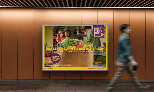 A person walking past a wall advertisement for Billa Online Shop. The ad features a brown paper bag with fresh groceries like lettuce, tomatoes, and bananas. The text promotes easy online shopping with a free 30-minute delivery offer. The background shows a kitchen scene with people.