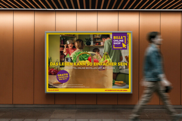 A person walking past a wall advertisement for Billa Online Shop. The ad features a brown paper bag with fresh groceries like lettuce, tomatoes, and bananas. The text promotes easy online shopping with a free 30-minute delivery offer. The background shows a kitchen scene with people.
