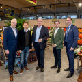Five men standing together in a grocery store, dressed in business casual attire, surrounded by fresh produce displays and baskets of fruit.