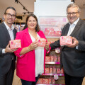 Three people smiling while holding packages of feminine hygiene products in a store. They stand in front of a display promoting the products.