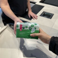 A person handing a package of sanitary pads across a counter to another person in a store setting.