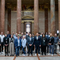 A group of people standing together in a grand hall with ornate columns and classical architecture. Several individuals are wearing badges and lanyards, suggesting a formal or professional gathering.