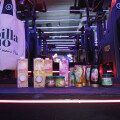 Assorted Billa Bio products, including beverages and jars, displayed on a gym floor with exercise bikes in the background. A Billa Bio tote bag is shown on the left.