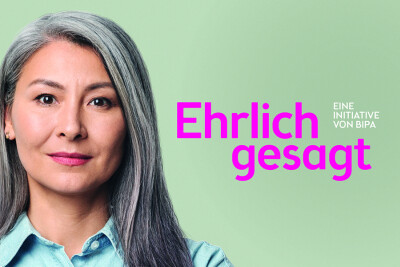 A person with long gray hair and a denim shirt against a light green background. Large pink text reads "Ehrlich gesagt," with smaller text "Eine Initiative von Bipa" in white.