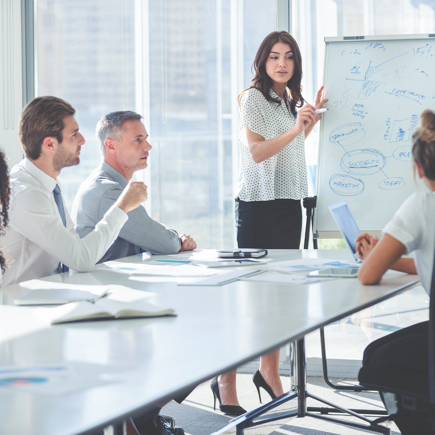 Frau steht bei einem Meeting vorne und schreibt auf das Flipchart
