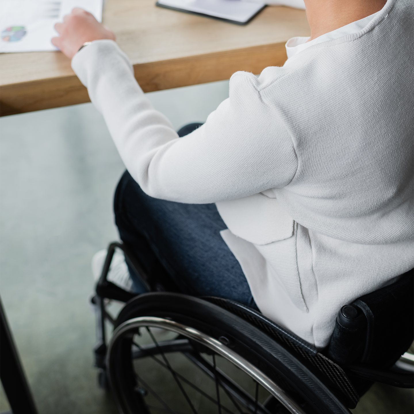 Person sitzt mit einem Rollstuhl am Meetingtisch